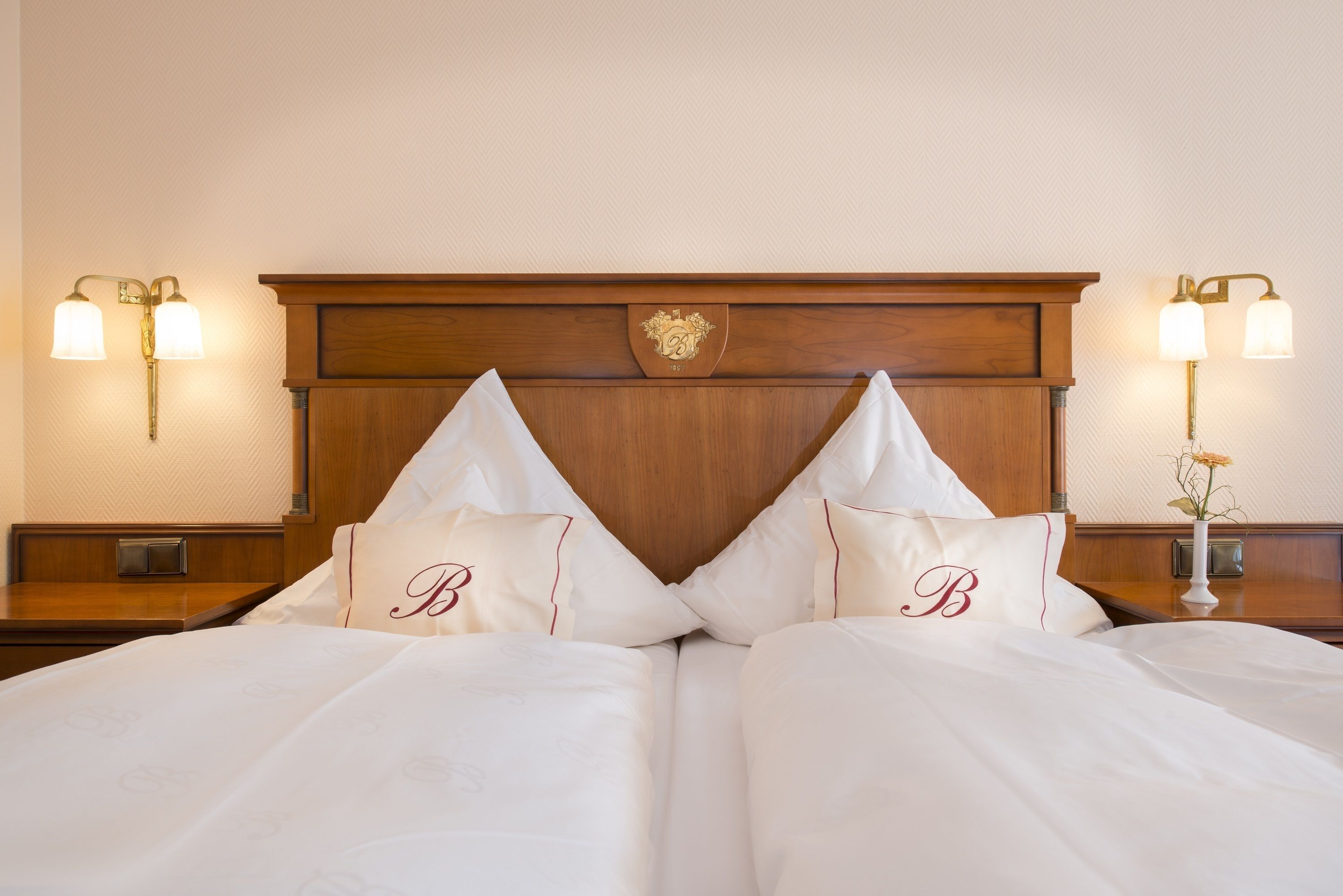 A neatly made bed with two pillows, a wooden headboard, and wall-mounted lamps.