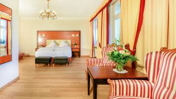 A hotel room with a large bed, a sofa, a table with a vase of flowers, and a chandelier.