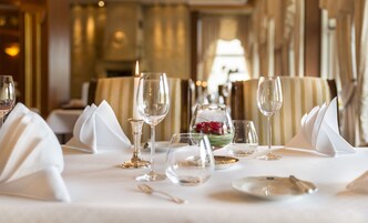 Una mesa de comedor servida con servilletas blancas, copas de vino y una vela.