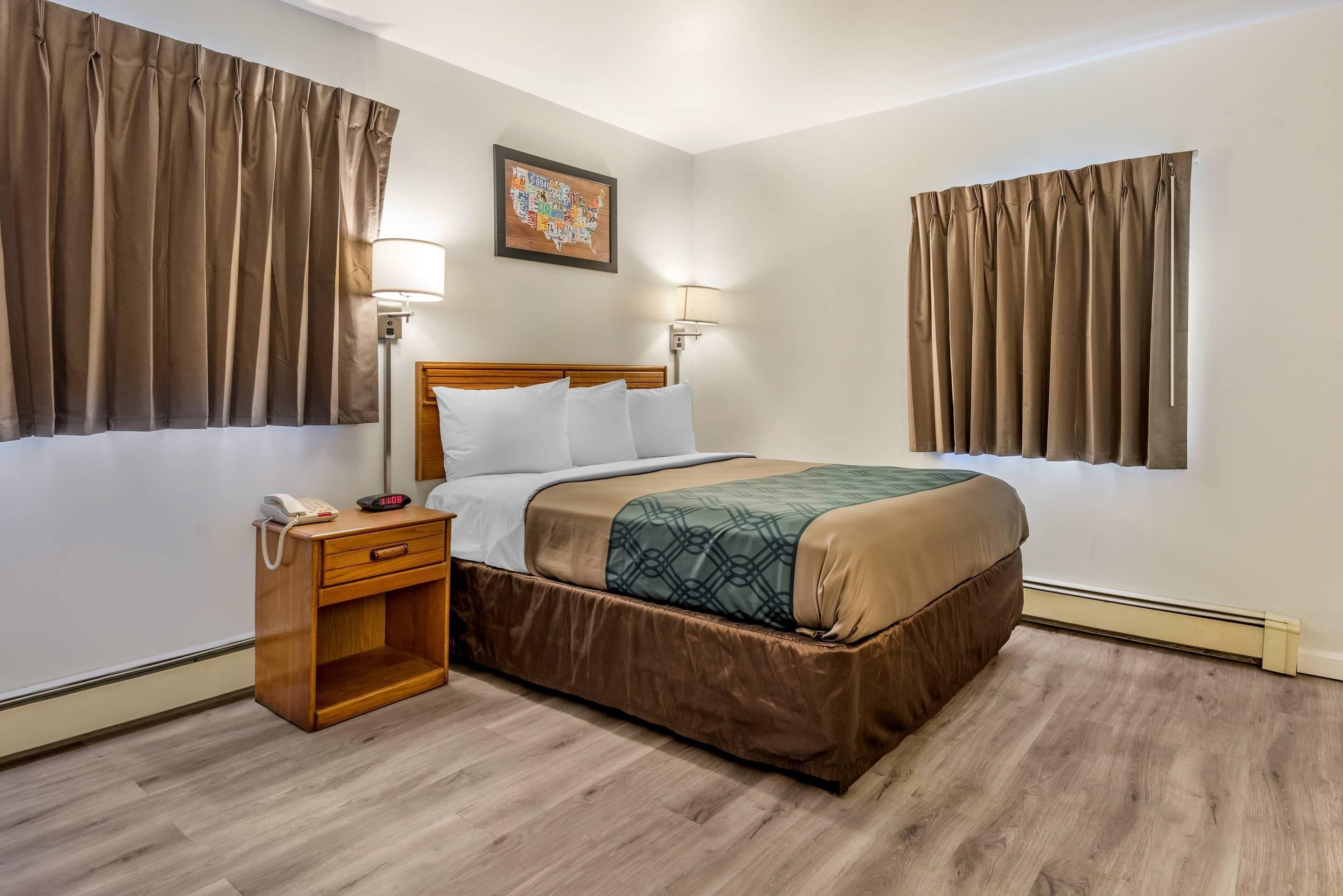 A hotel room with a wooden bed, a nightstand with a phone, two wall-mounted lamps, and a map on the wall.