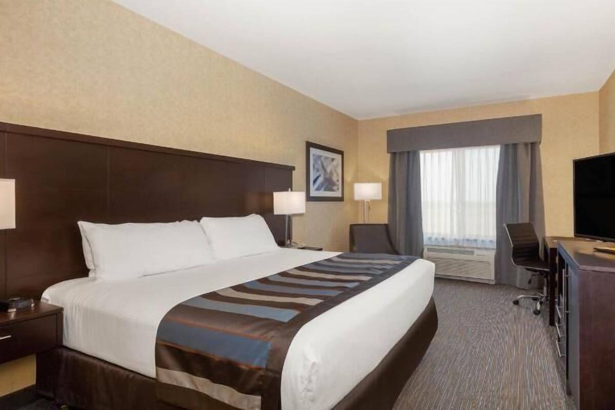 A hotel room with a large bed, a desk with a television, a chair, and a window with curtains.