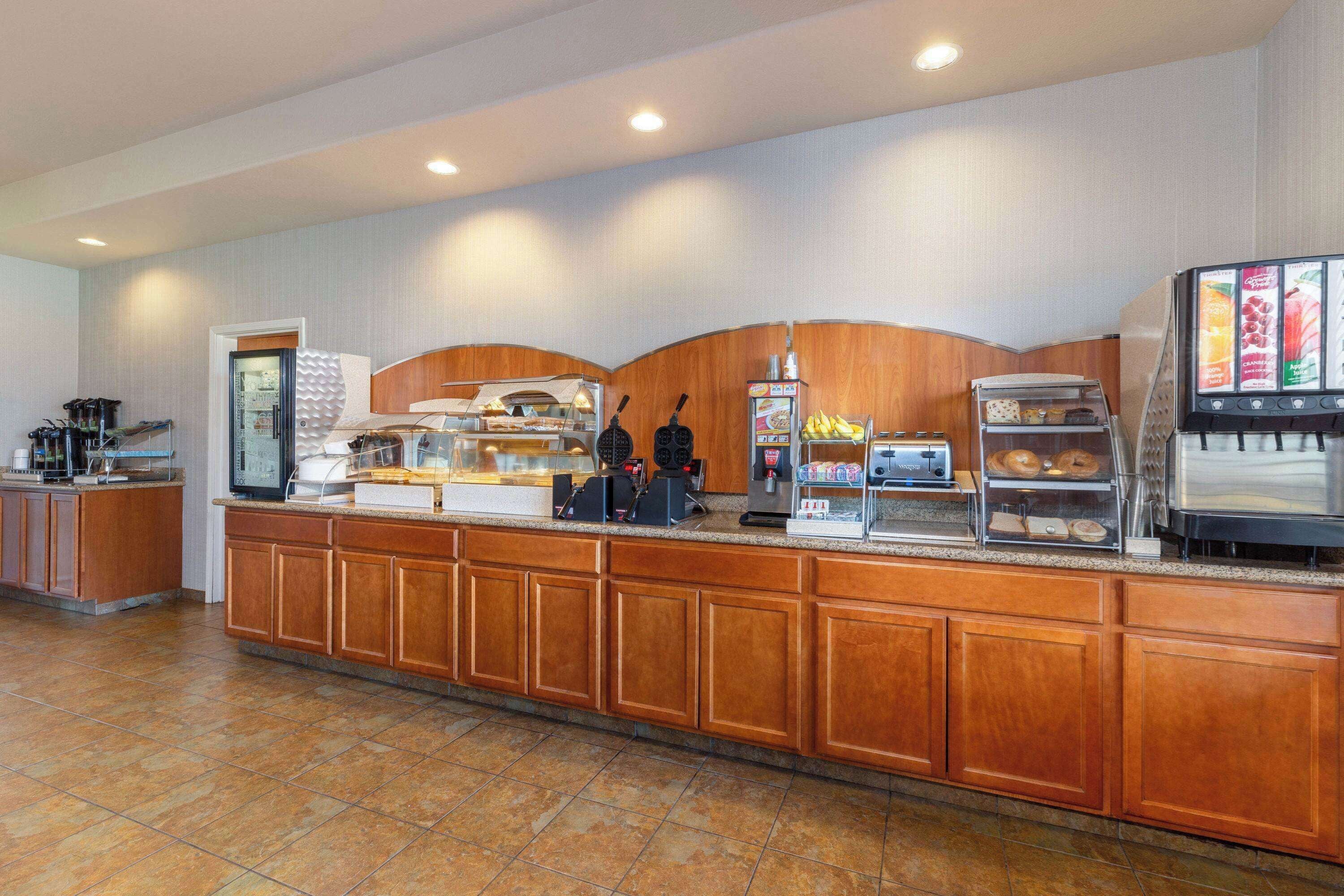 Un mostrador de buffet con distintas estaciones de comida, que incluyen una máquina de café y una vitrina con pasteles.
