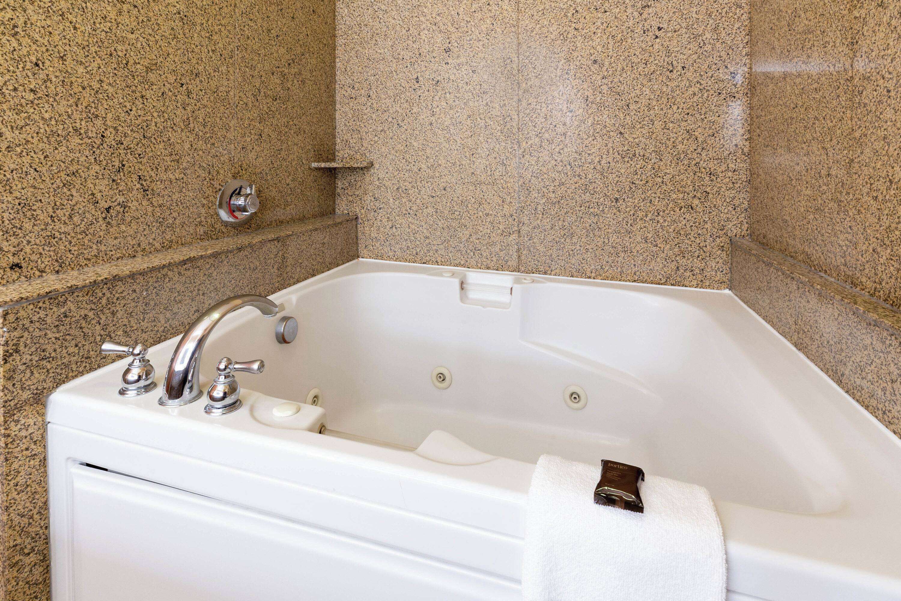 A white bathtub with a single faucet and a soap dish, set against a speckled granite wall.