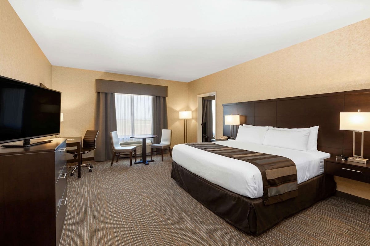 A hotel room with a bed, a desk with a TV, a chair, a table, and a lamp.