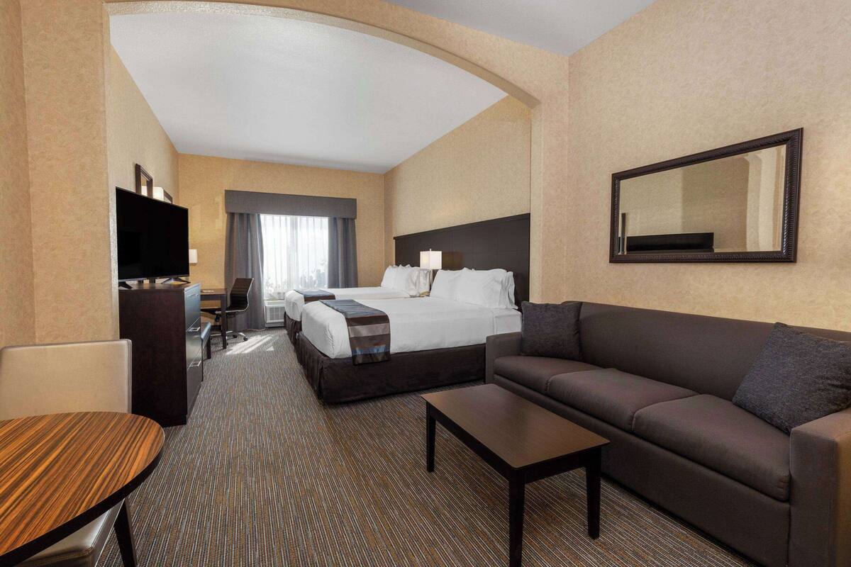 A hotel room with a bed, a sofa, a desk, a television, and a mirror.