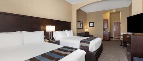 Habitación de hotel con dos camas, un escritorio, un televisor y un baño visible a través de un arco.