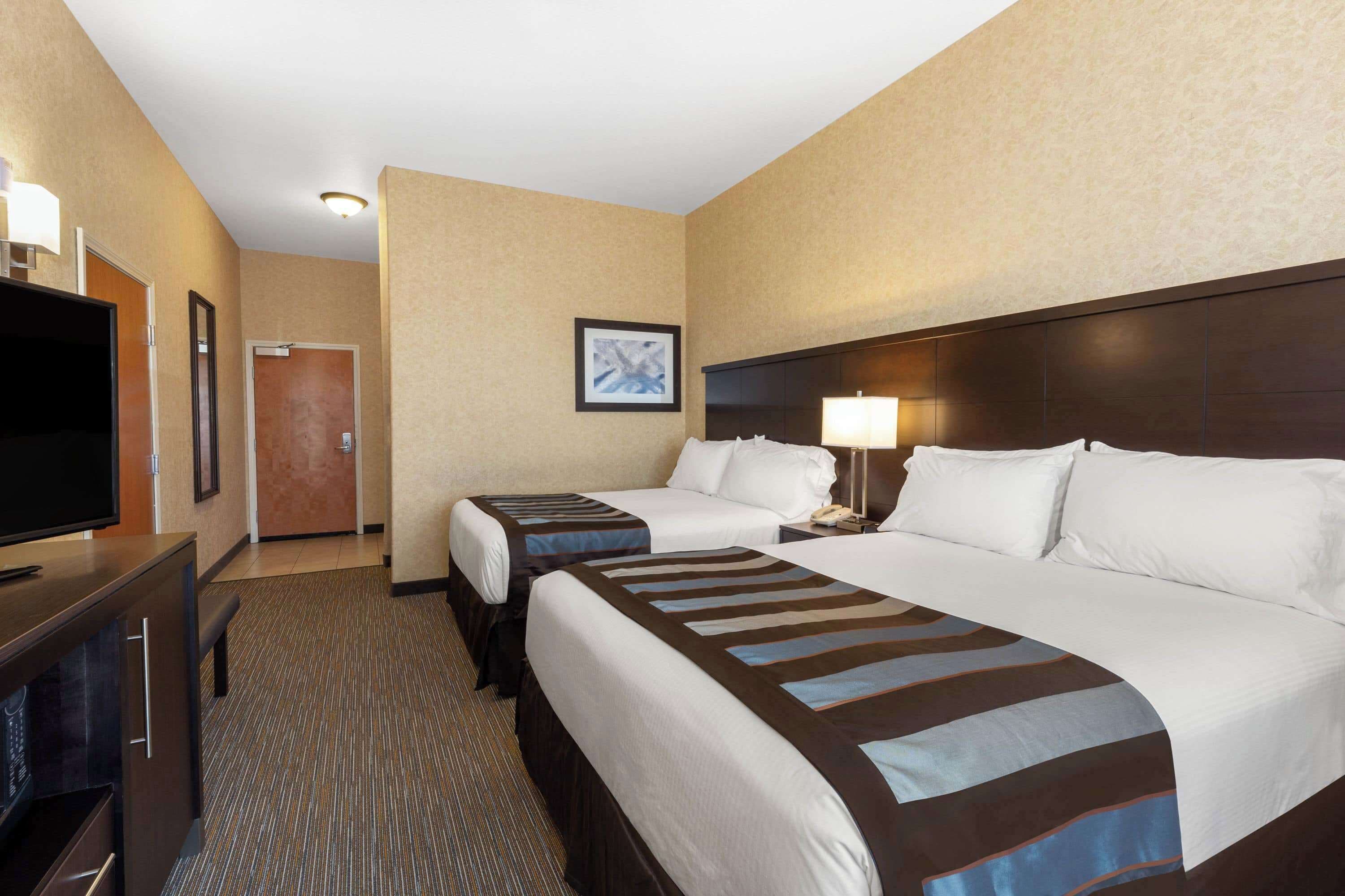 A hotel room with two beds, a TV, a desk, and a framed picture on the wall.
