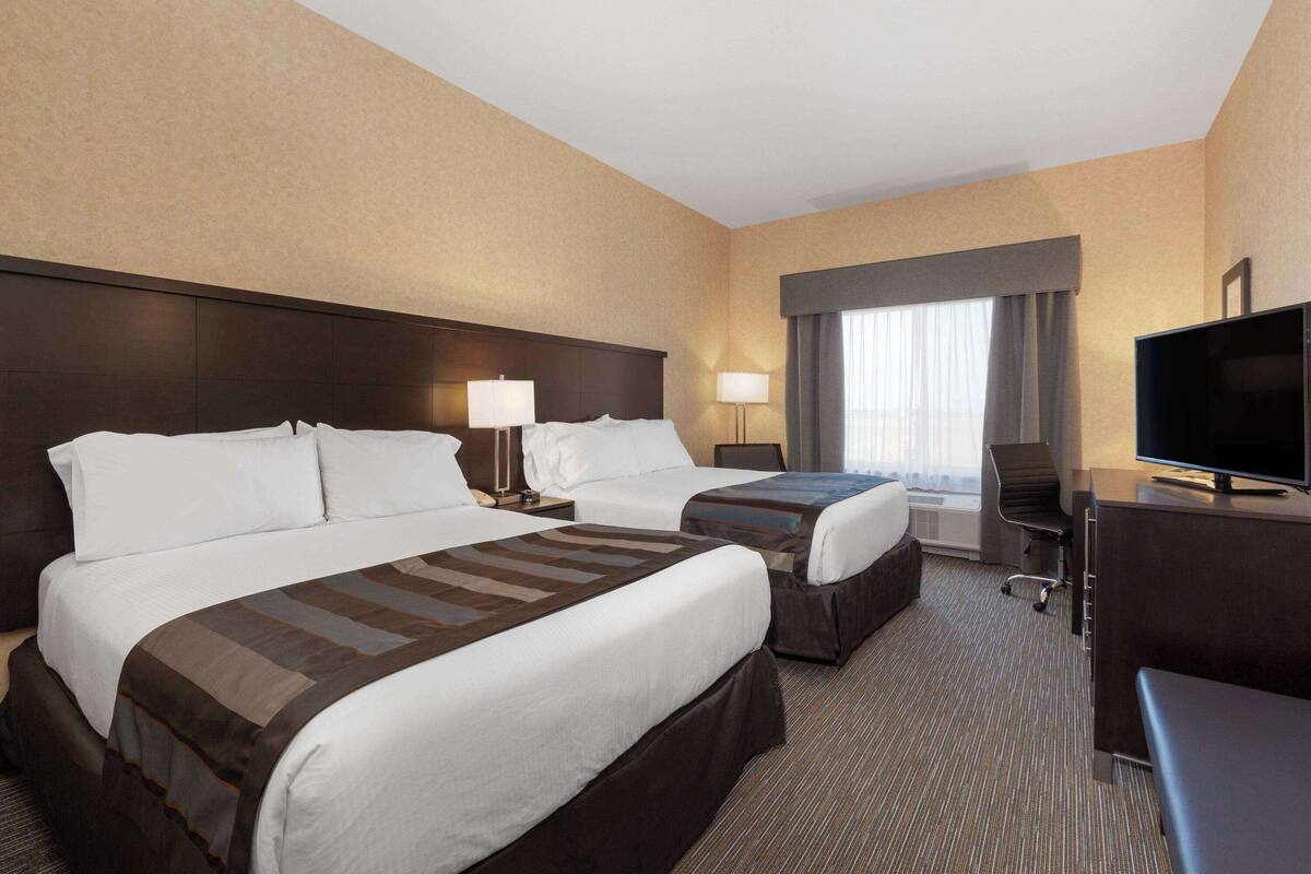 A hotel room with two beds, a desk, a television, and a window with curtains.