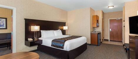 A hotel room with a large bed, bedside tables, a desk, a chair, a TV, and a small kitchenette.