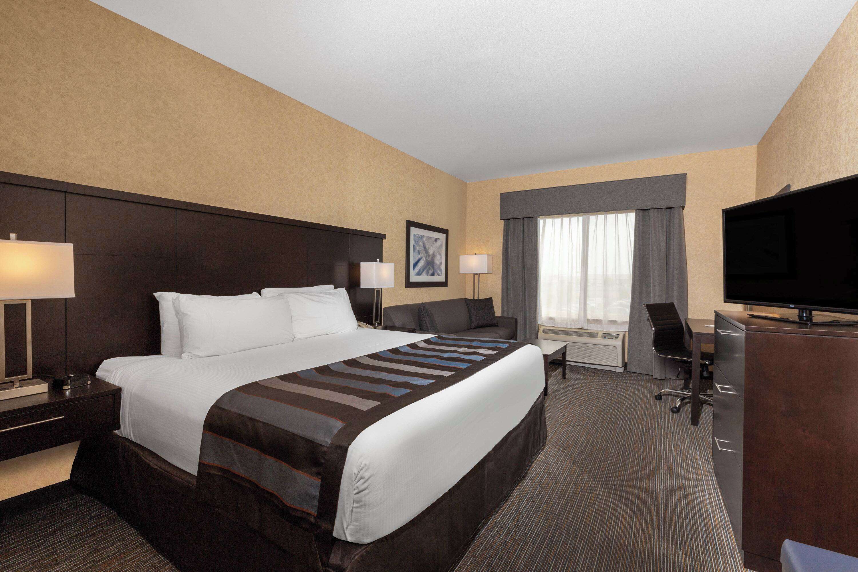 Une chambre d’hôtel avec un grand lit, un bureau, une chaise, une télévision et une fenêtre avec des rideaux.