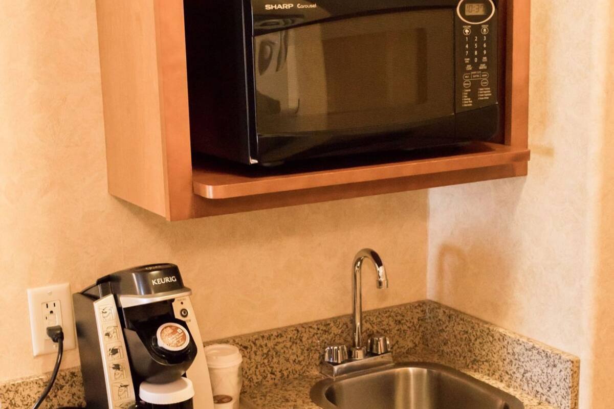 A compact kitchenette with a microwave, coffee maker, sink, and dishwasher.