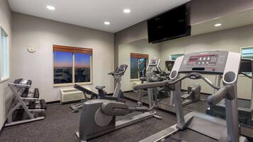 Un gimnasio con máquinas de cardio, mancuernas y un televisor en la pared.