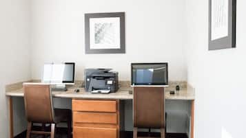 Espaço de trabalho em hotel com duas mesas, cada uma com monitor de computador, impressora e cadeira.