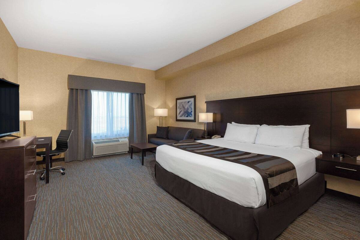 A hotel room with a large bed, a desk, a chair, a TV, and a window with curtains.
