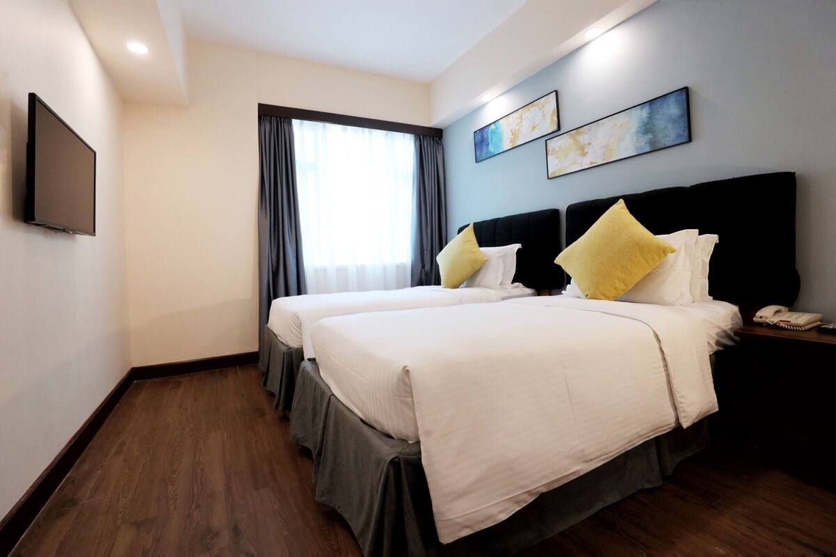 A hotel room with two beds, a flat-screen TV mounted on the wall, and a window with curtains.