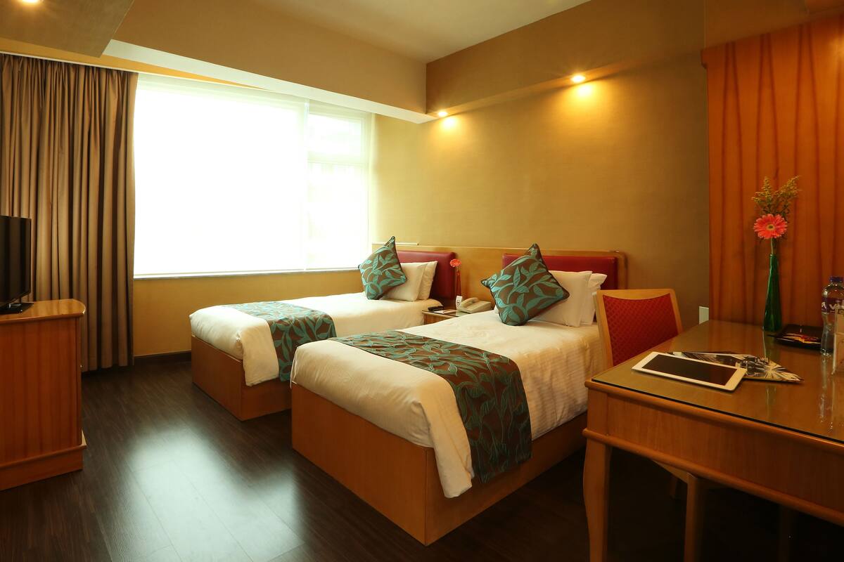A hotel room with two beds, a TV, a desk, and a window with curtains.