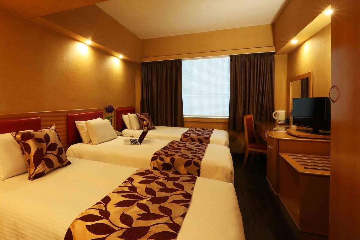 A hotel room with two beds, a desk with a computer, and a window with curtains.