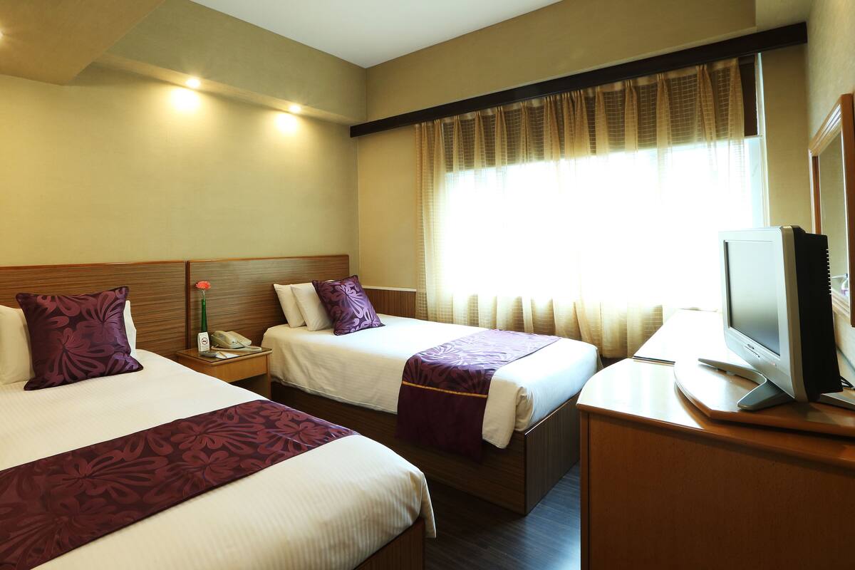 A hotel room with two beds, a desk with a computer, and a window with curtains.