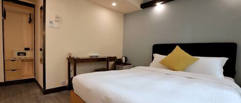 A hotel room with a bed, bedside table, and a desk with a chair.