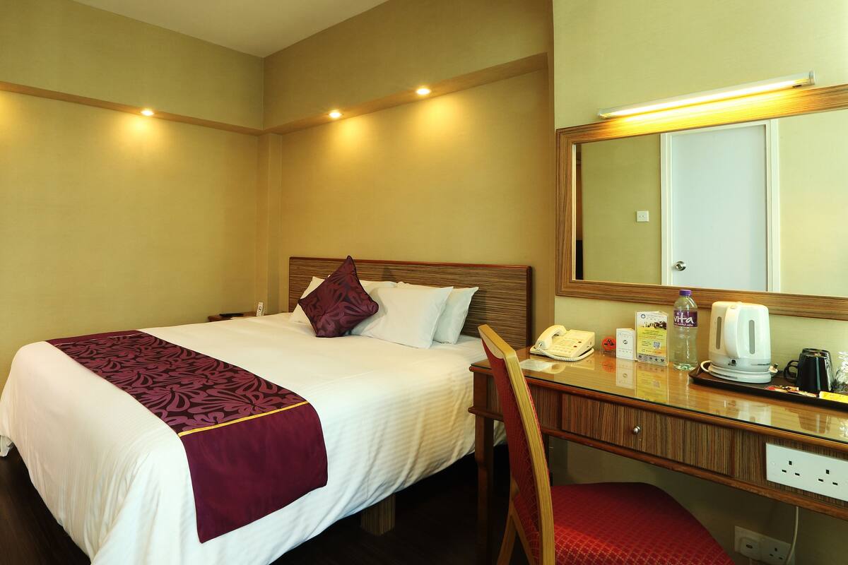 A hotel room with a bed, bedside table, mirror, and a red chair.