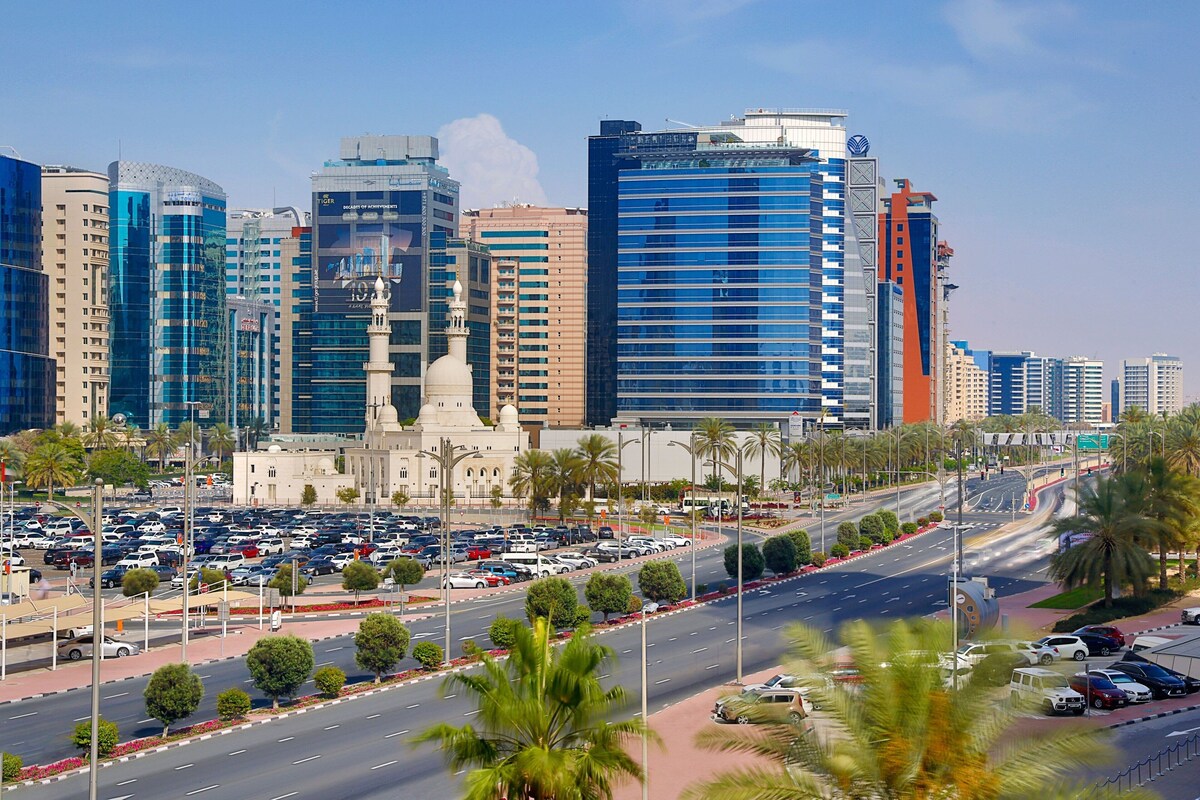Un paisaje urbano con edificios modernos, una mezquita y una transitada calle con coches y palmeras.