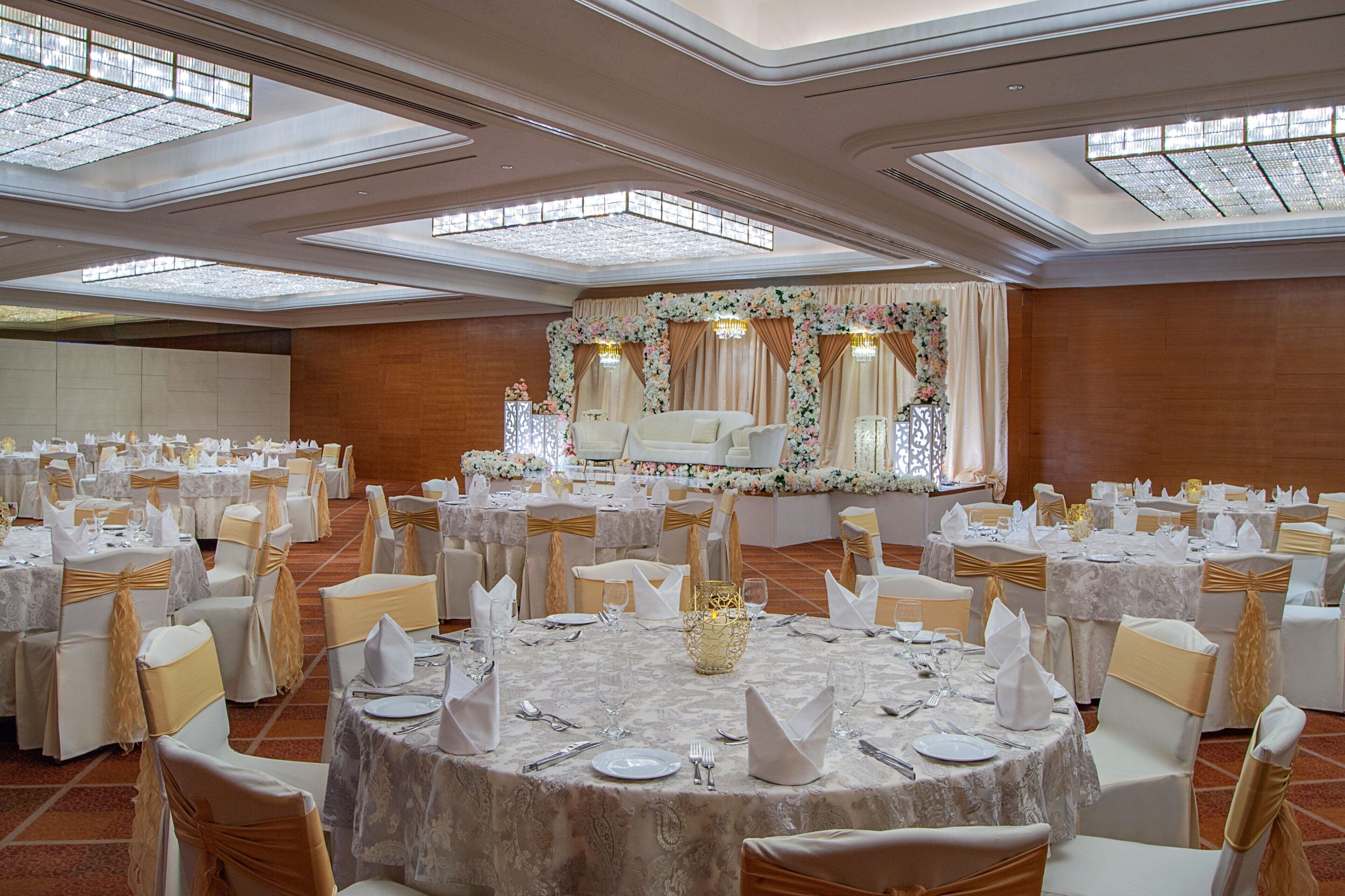 Un salón de banquetes con mesas redondas, sillas blancas y decoración floral.