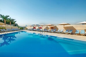 A swimming pool with lounge chairs and umbrellas, surrounded by palm trees and a clear sky. - Sheraton Dubai Creek Hotel & Towers (Dubai)