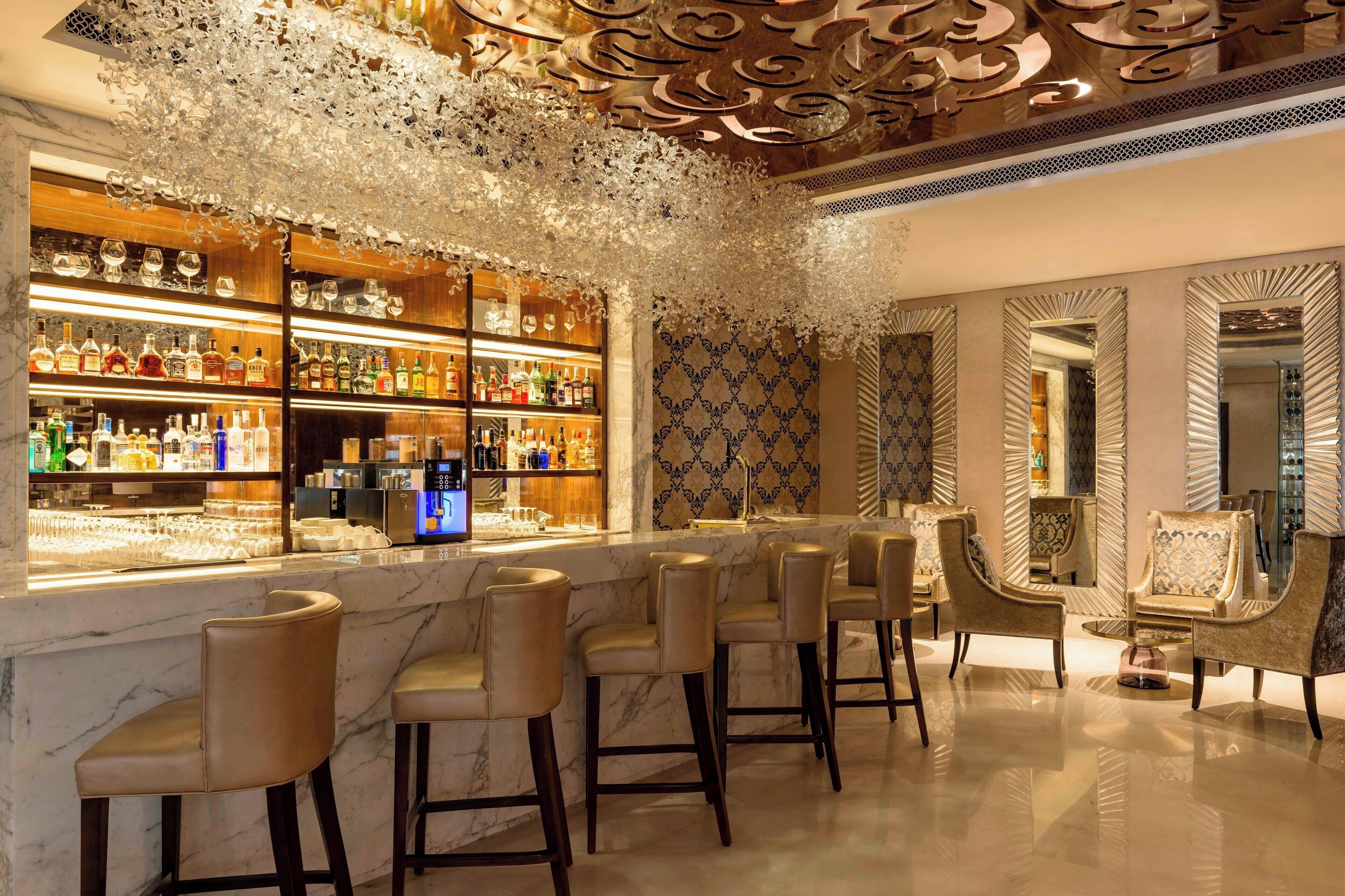 A bar area with marble countertops, multiple bar stools, and a variety of bottles and glasses.