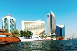 A waterfront view with a modern building, a traditional boat, and other boats docked nearby. - Sheraton Dubai Creek Hotel & Towers (Dubai)