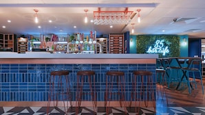 Eine Bar mit Hockern, einem Neonzeichen und einer Auswahl an Flaschen und Gläsern auf Regalen.