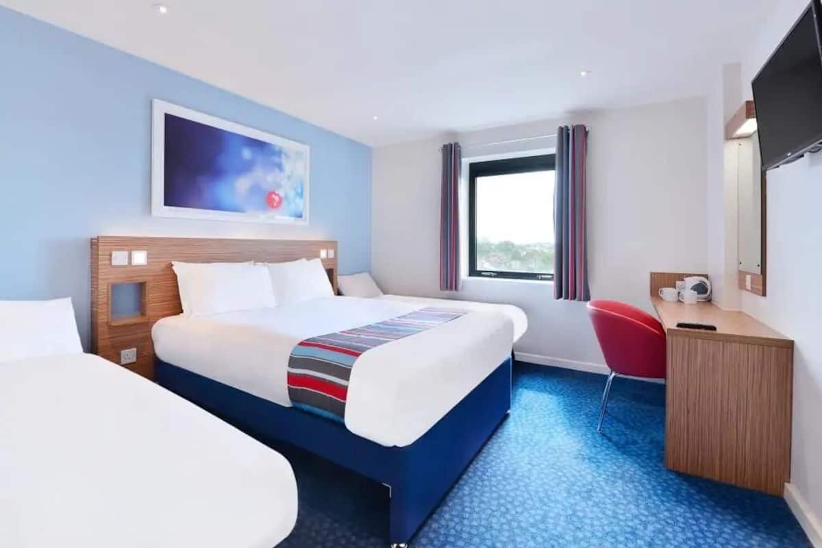 Une chambre d’hôtel avec un grand lit, un bureau, une chaise, une télévision et une fenêtre avec des rideaux.