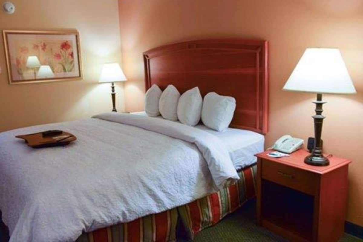A hotel room with a bed, two bedside lamps, a nightstand with a phone, and a painting on the wall.