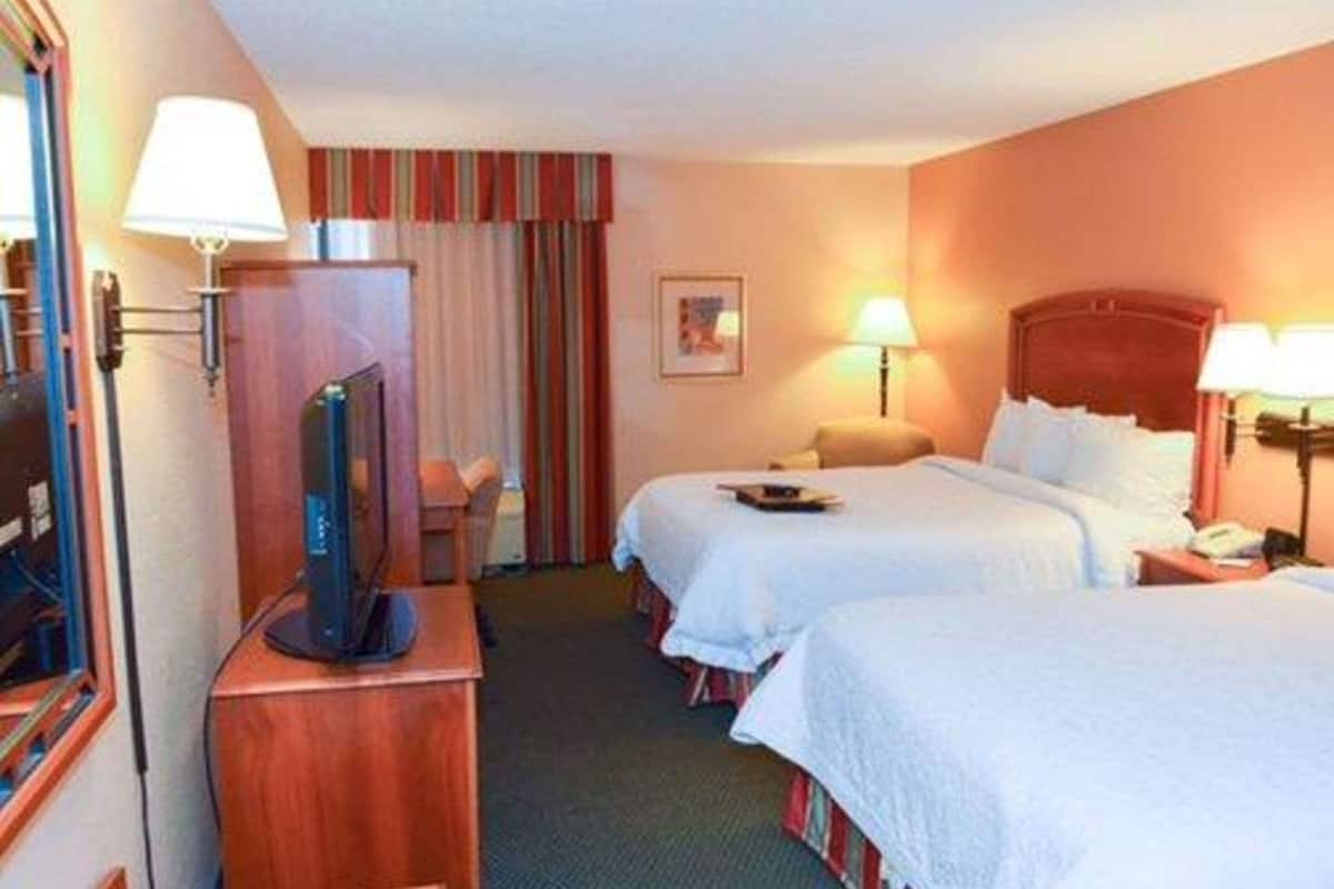 A hotel room with two beds, a desk with a television, a chair, and a window with curtains.