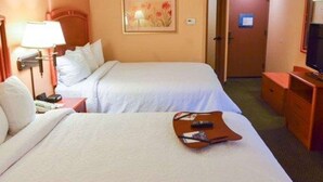 Habitación de hotel con dos camas, un escritorio con lámpara, televisor y un cuadro en la pared.