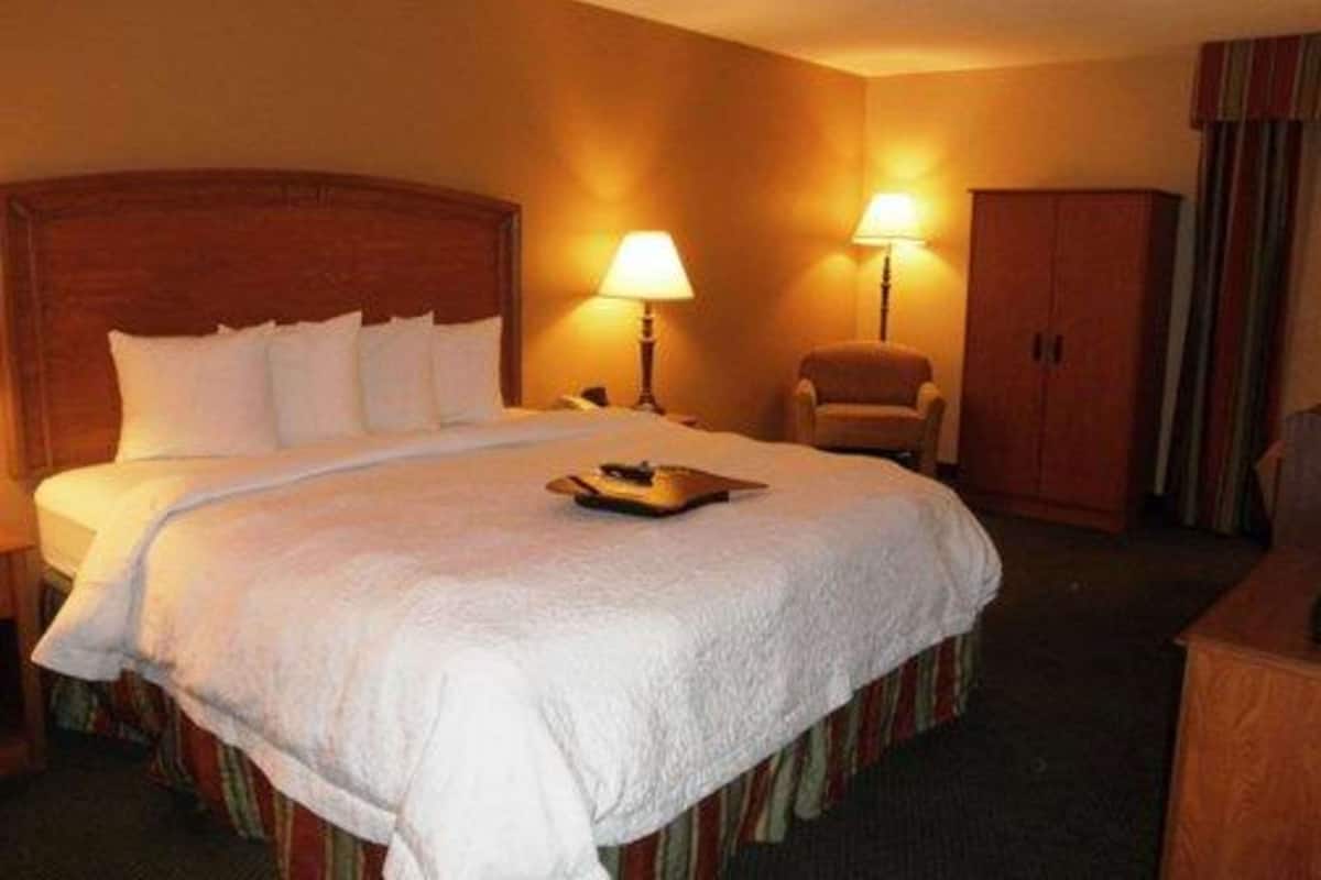 A hotel room with a large bed, two bedside lamps, a chair, and a wardrobe.