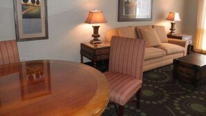 Una habitación de hotel con una mesa de comedor redonda de madera, un sofá, dos lámparas y cuadros en las paredes.