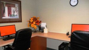 Un espacio de trabajo con dos escritorios, dos computadoras, un reloj y un cuadro en la pared.