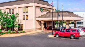 Un hotel con fachada color beige, un letrero que dice claramente “Quality Inn” y un estacionamiento con un coche rojo.