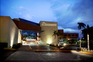 Entrada de un hotel Marriott al anochecer, con un diseño moderno, un corredor cubierto y palmeras.