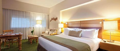 Habitación de hotel con una cama grande, un escritorio, una silla, una lámpara y una ventana con cortinas.