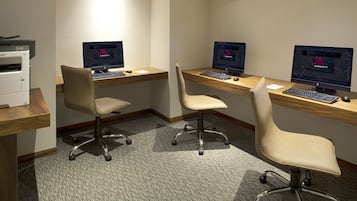 A hotel room with three desks, each with a computer monitor, keyboard, and mouse. There is a printer on the left side of the room.