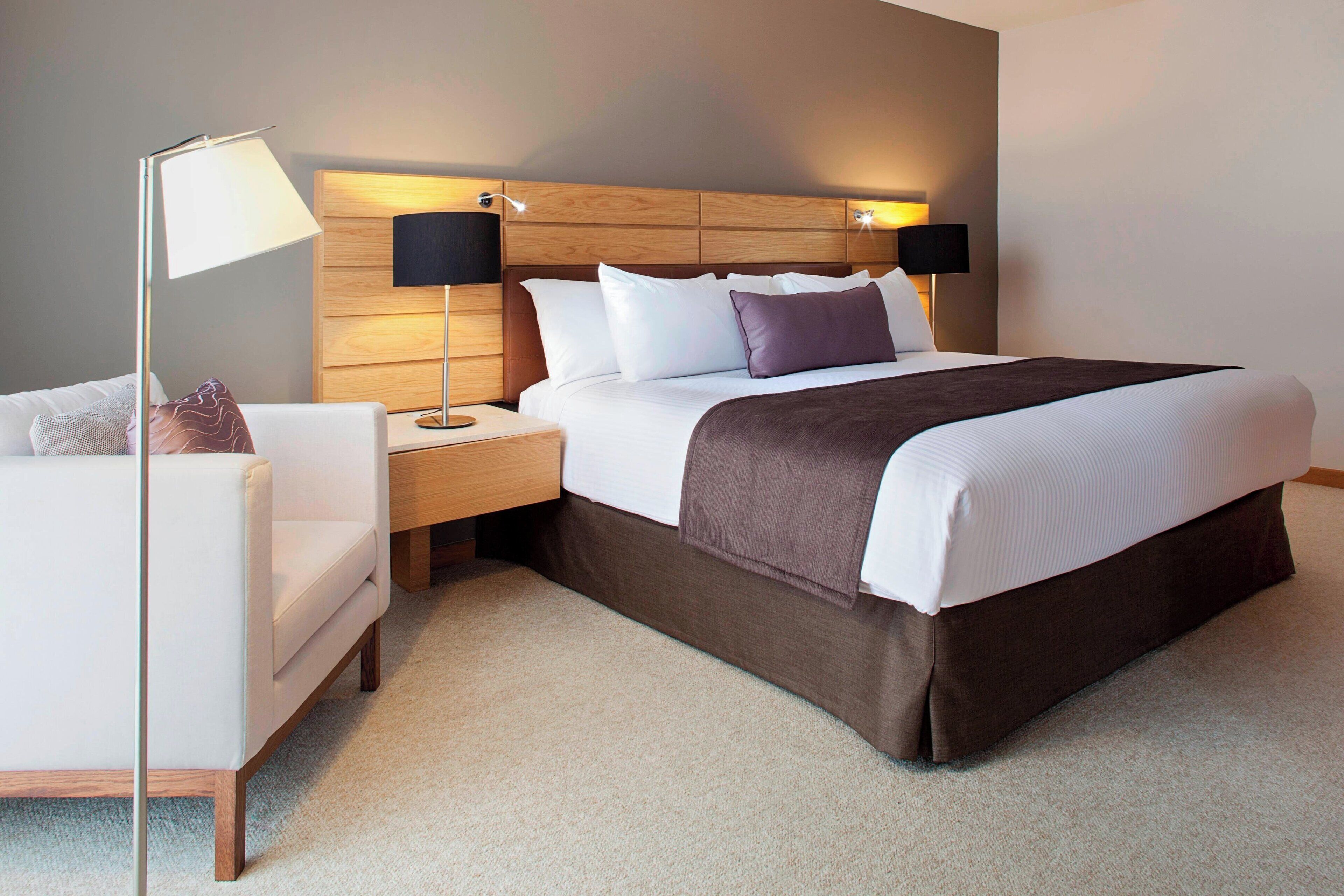 A hotel room with a bed, bedside tables, a lamp, and a chair.