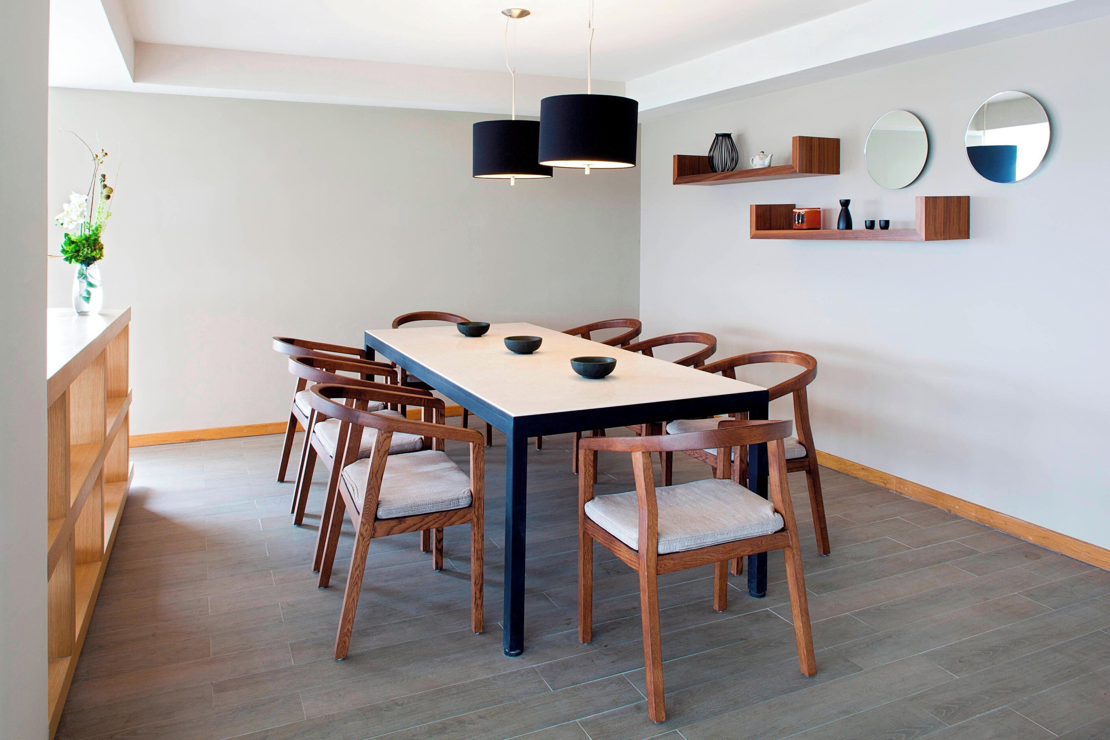 A dining area with a long table, six wooden chairs, and two pendant lights.
