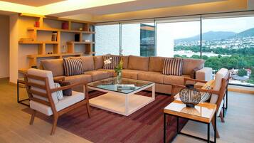A modern living room with a large sectional sofa, a glass coffee table, and a view of a cityscape through large windows.