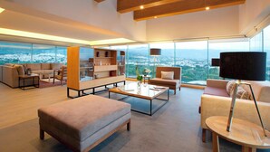 Un amplio salón con un gran ventanal que ofrece vistas a la ciudad, techo de madera y muebles modernos.