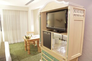 A hotel room with a television on a cabinet, a dining table with a chair, and a window with blinds.