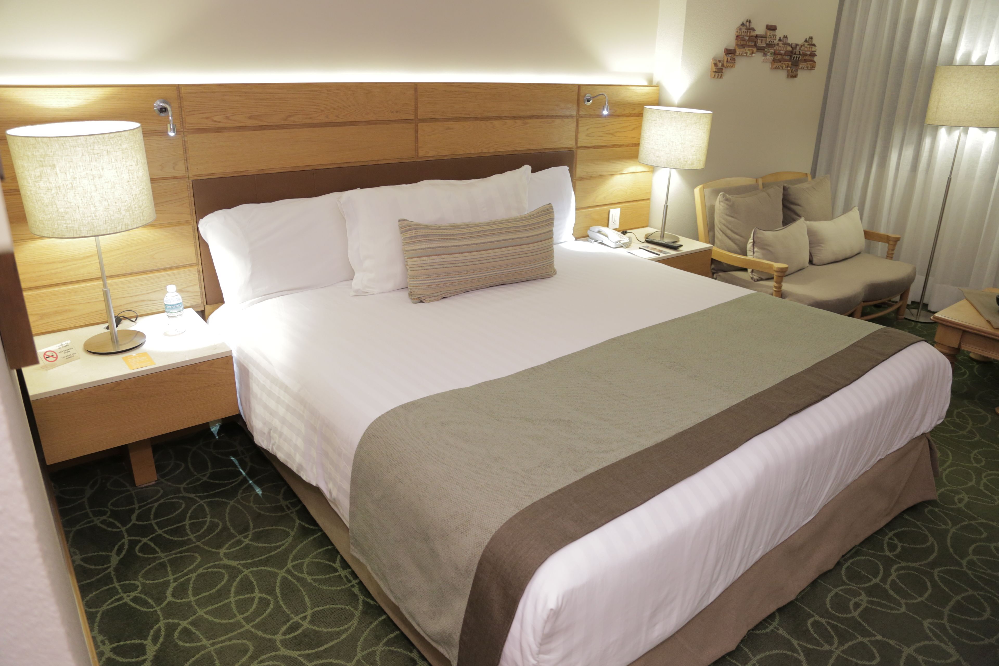 A hotel room with a large bed, two bedside tables, a chair, and a lamp.