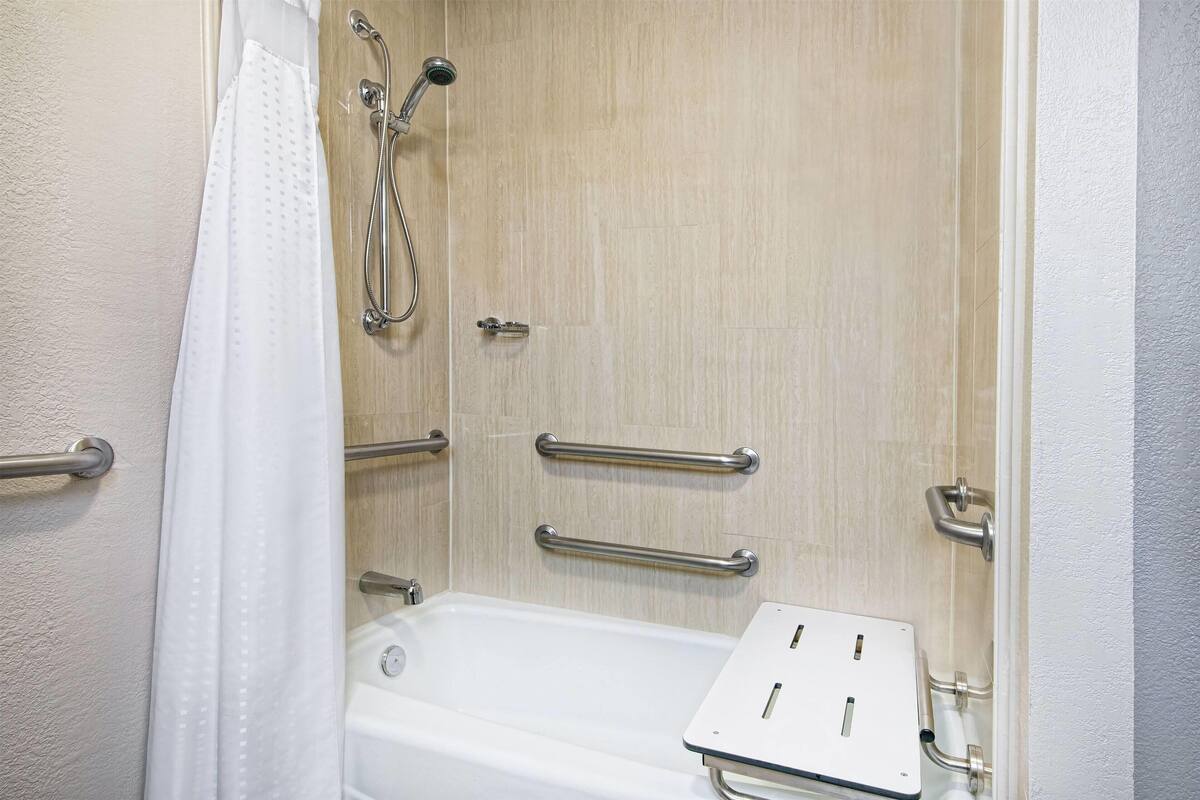 A bathroom with a bathtub, grab bars, and a shower head.