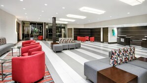 A modern lobby with red and grey seating, a patterned rug, and a large glass door leading outside. - Wyndham Houston Sugarland (Houston)