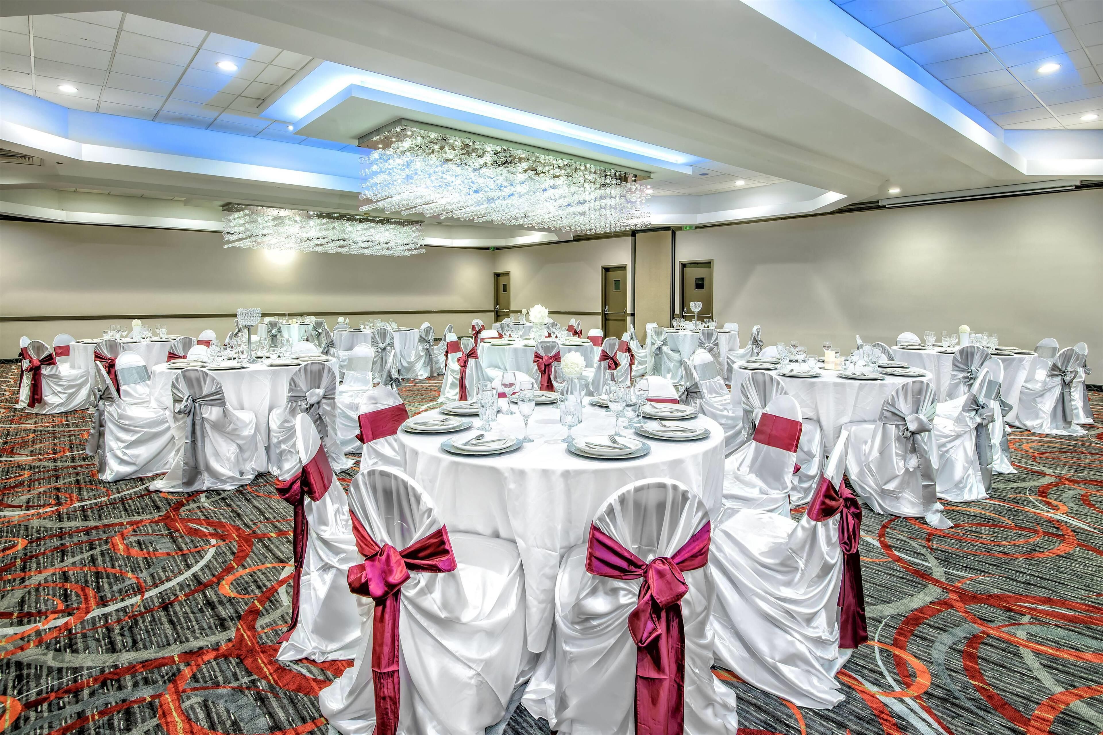 A banquet hall with round tables set for events, featuring white tablecloths and chairs with pink sashes.